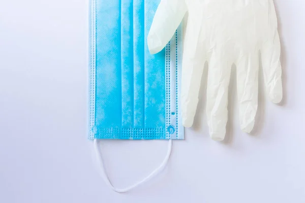 Medical disposable blue mask and a one of white latex gloves lie on a white background. Necessary protective equipment for a doctor or a simple person from viruses. Concept. Covid-19, coronavirus.