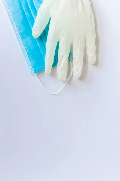 Tıbbi tek kullanımlık mavi maske ve beyaz arka planda duran beyaz lateks eldivenlerden biri. Bir doktor ya da virüslü basit bir insan için gerekli koruyucu ekipman. Kavram. Covid-19, koronavirüs..