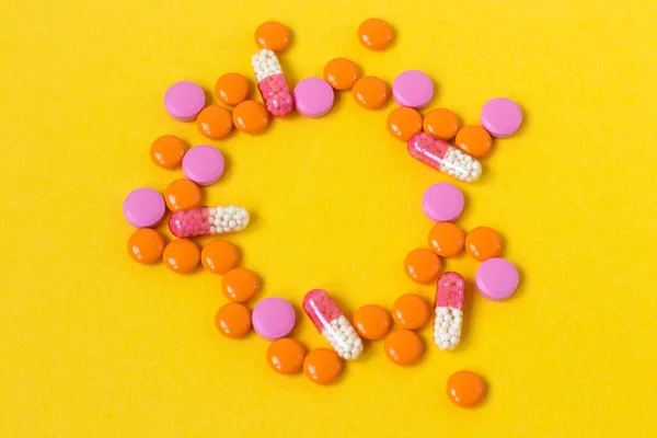 Multi-colored pills in the form of a female egg on a bright yellow background, top view. Medication for the disease for patients. Dose drugs and vitamins for health. Copy space. Close up.