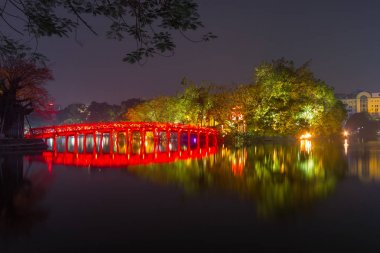 Beautiful night view of the Huc Bridge over Hoan Kiem Lake leads to Ngoc Son Temple on a small island (Original built in 1841) with cityscape background, Hanoi, Vietnam clipart