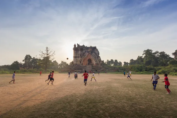 Mandalay, Myanmar - Şubat 18,2018: Birmanya kişi antik pagoda ile sahada futbol oynayan günbatımı, Inn Wa City, Mandalay, Myanmar sırasında arka planda Harabeleri