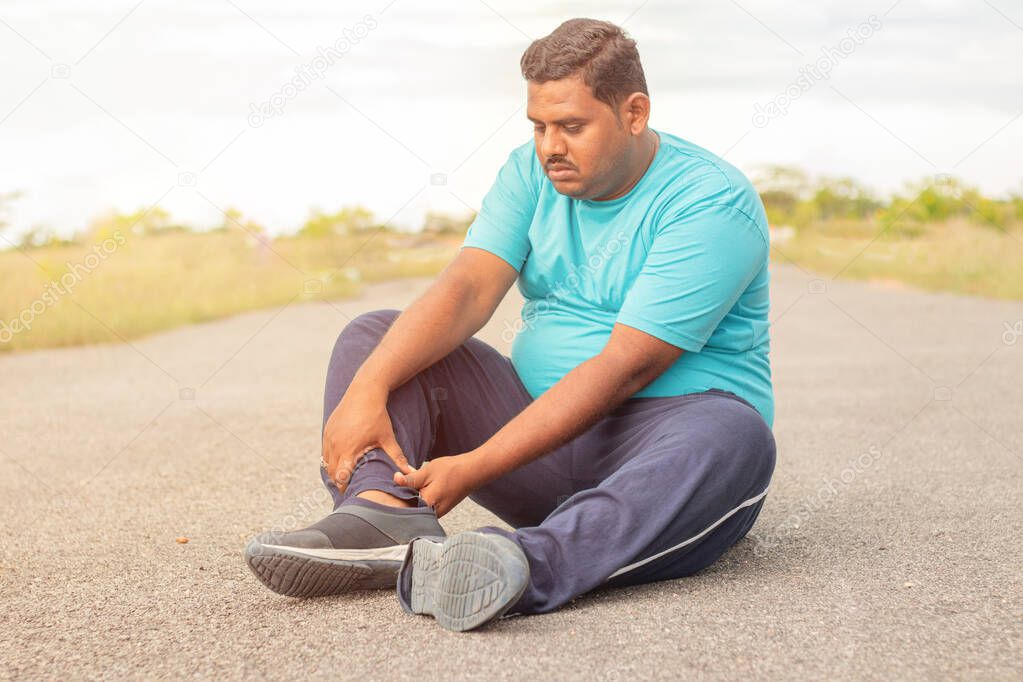 Concept of leg tendon injury of fat man - obese person holding leg suffering muscle pain - overweight man fitness concept at outdoor park.
