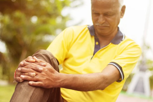 Hombre mayor con una lesión en la rodilla - Concepto Senior Man fitness y yoga al aire libre - Enfoques selectivos en la mano, anciano sosteniendo la rodilla debido al dolor . — Foto de Stock