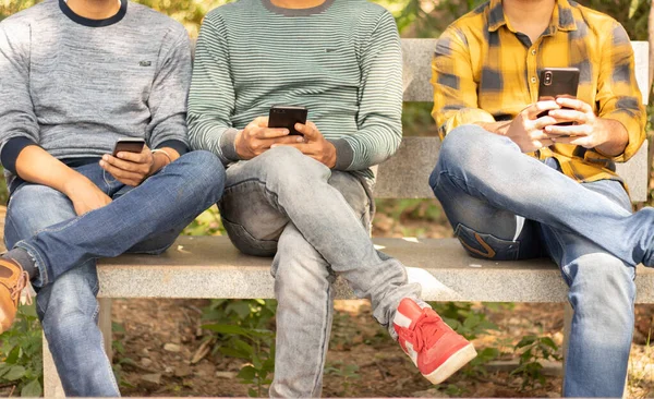 Unga män upptagen på mobilen medan du sitter på bordet i parken - Begreppet ung generation beroende av smartphone, teknik och elektroniska prylar - Begreppet modern ungdom livsstil, Social interaktion. — Stockfoto