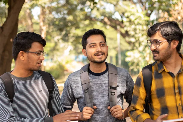 Three students talking or socializing at university campus - Friends having fun and conversation at college - concept of happy friendship, college days and student life.