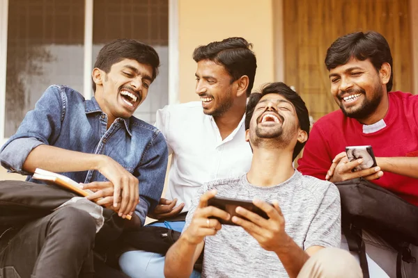 Grupp glada unga collegestudenter genom att titta på mobiltelefon skrattar högt på universitetsområdet - Millennials njuter online videoinnehåll eller sociala medier genom att titta på smarttelefon. — Stockfoto