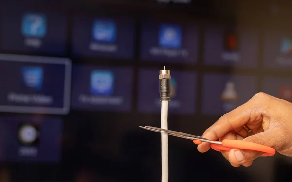 Maski, India 18,January 2020 - Hand cutting TV cord in from of the Smart TV showing different Streaming services in out of focus as a background