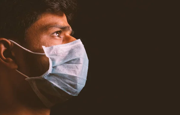 Jovem usando máscara facial médica para proteger contra a propagação de infecção por surto de coronavírus na sala escura e pensando em ataque de vírus . — Fotografia de Stock