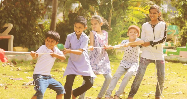 Group of multi racial children playing Tug of war game kindergarten - Multi ethnic kids playing outdoor games against racism.