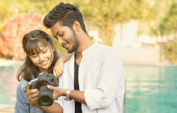 Linda pareja mirando imágenes en la pantalla de la cámara - Feliz joven fotógrafo profesional mostrando imágenes para modelar en su DSLR - concepto de modelo y camarógrafo trabajando juntos . — Foto de Stock