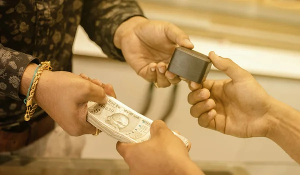 Close up of hands buying or purchasing gold jewellery by paying Indian currency at jewelry shop India - concept of gold investment for profit