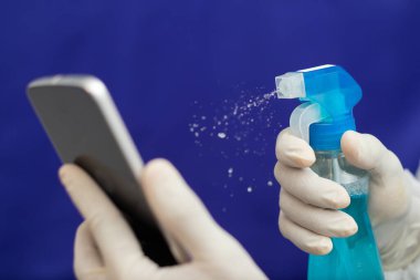 Covid-19 'u bertaraf etmek için Doktor Temizlik cep telefonu - Eldivenli hemşire elleri hastanede sıvı dezenfektanla telefonu temizliyor - Coronavirüs' le kirliliği temizlemek için alkol