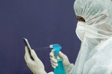 Coronavirüs ya da Covid-19 salgını salgını nedeniyle cep telefonunu sterilize eden bir doktor ya da mikropları ve virüsü yok etmek için cep telefonunu temizliyor.