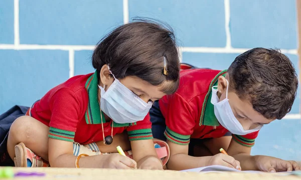 Kids busy in writing with medical face mask wearing due to covid-19 or coronavirus outbreak or pandemic at school - children painting at home during lockdown. — Stock Photo, Image