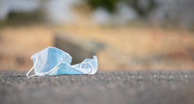 Atılmış tıbbi yüz maskesi yola yapışmış. Maskelerin hijyenik olmayan bir şekilde atılması, covid-19 veya coronavirüs salgılamasına yardımcı olur..