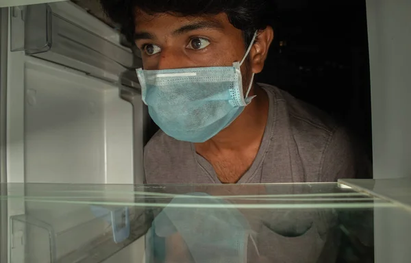 Человек в медицинской маске смотрит в пустой холодильник или холодильник для еды - Концепция не кладовой пищи доступны во время домашнего карантина в ковид-19 или коронавирус — стоковое фото