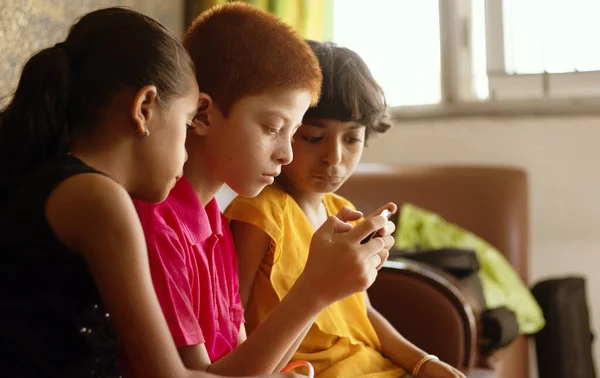 Three multi ethnic kids or siblings busy in playing games on mobile at home - concept of childrens mobile video game addiction, using technology, internet on smartphone. — Stock Photo, Image