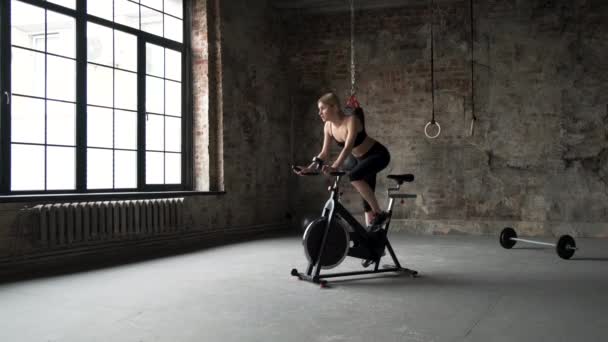 年轻活跃的女人在健身房骑自行车放松 女子慢动作自行车训练 在健身房工作的健身女孩中枪 — 图库视频影像