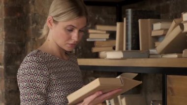 Genç bir kadın kütüphaneden bir kitap seçiyor. O, kitapların arasında koridorda. Genç bir kadın kütüphaneden bir kitap seçiyor.. 