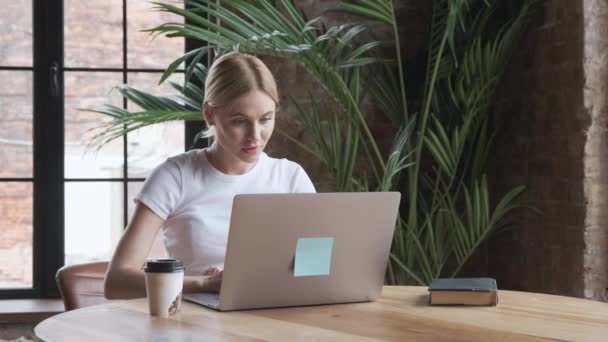 迷人的年轻女性自由职业者一边在笔记本电脑上工作一边喝咖啡或喝茶 — 图库视频影像