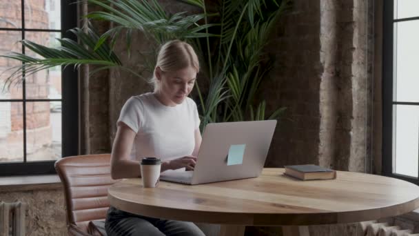 迷人的年轻女性自由职业者一边在笔记本电脑上工作一边喝咖啡或喝茶 — 图库视频影像