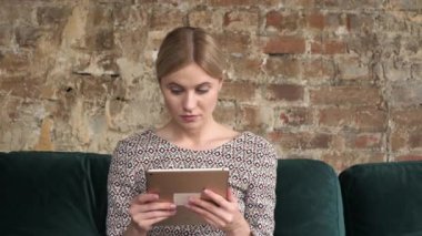 Kadın kanepede oturuyor, tablet bilgisayar kullanıyor. Evde dijital tablete dokunan bir kadın var. Evde tablet kullanan kadın, teknolojiyi kullan