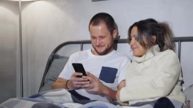 Karı koca akıllı telefon kullanarak evde oturup gülüyorlar.