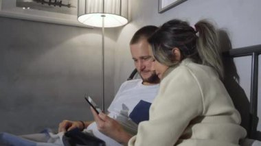 Kafkasyalı karı koca pijamalarıyla geceleri sessizce yatakta oturuyorlar, yatak başlığına yaslanıyorlar, akıllı telefonlar tutuyorlar ve tamamen dalmış görünüyorlar.
