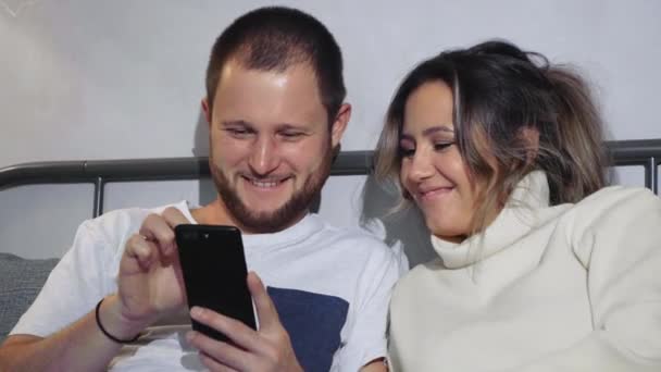 Mutlu Genç Bir Çift Cep Telefonlarına Bakarken Evde Yatakta Uzanıyorlar — Stok video