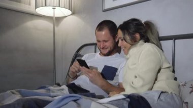 Sosyal medya ağlarına bağımlı bir çift, yatakta birlikte vakit geçirip akıllı telefonlarıyla herkese sarılıp mesajlaşıyor.