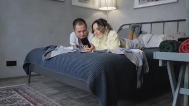 Otel yatağında genç bir çift akıllı telefondan mesajlar okuyor ve gülüyor.