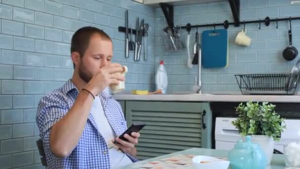 Młody Szczęśliwy Człowiek Rozmawiający Smartfonie Pijący Herbatę Popołudniowych Przerwach Salonie — Wideo stockowe