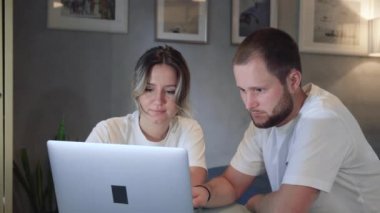 Ciddi genç çift, internet üzerinden faturalarını ödüyor. Evrak işleri planlama bütçesi, finansman, ipotek ödemeleri, dizüstü bilgisayar, mutfak masasında oturuyor.