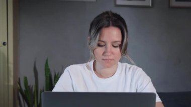 Evde dizüstü bilgisayarında çalışan kıvırcık saçlı, serbest çalışan genç kadın portresi. Esmer kız bilgisayarında masanın yanında bir şey yazıyor. Serbest meslek kavramı.