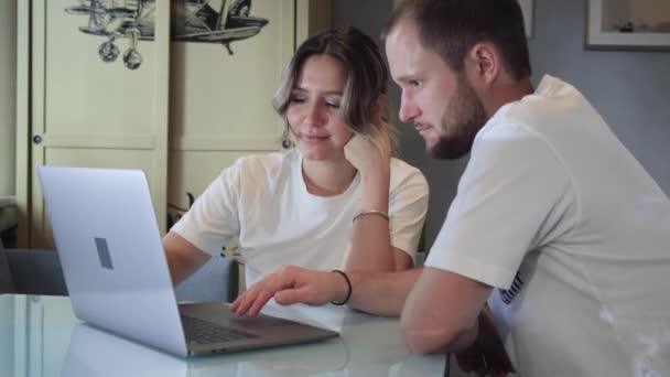 快乐的年轻夫妇用笔记本电脑电子商务 一起上网购物 一起看视频电影 微笑的男人和在家里看着电脑的高加索女人 — 图库视频影像