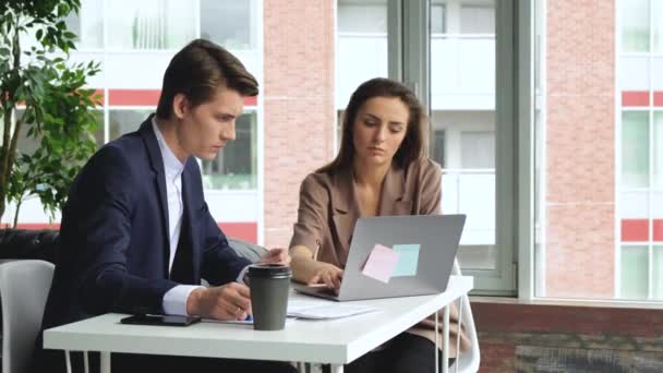 男と女は現代のオフィスのノートパソコンで働いている チームワークコンセプト4K 締め切り コーヒーと書類付きの従業員デスク — ストック動画