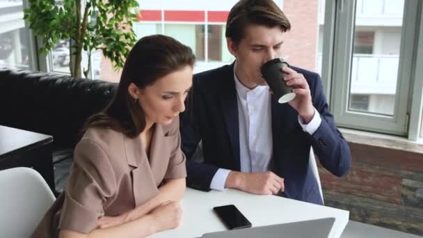 Mladý muž a žena diskutovat. Muž ukazuje detaily na obrazovce Žena naslouchá Držení šálek kávy v jejích rukách.Jejich kancelář je vývojář a moderní vzhled.