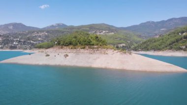 Temiz yeşil suyu ve kıyı manzarasında büyük taşları olan güzel bir dağ gölü. Kıyı şeridinde uçan drone oyuğundan manzara. Yeşil dağların arasında kayalık nehir..
