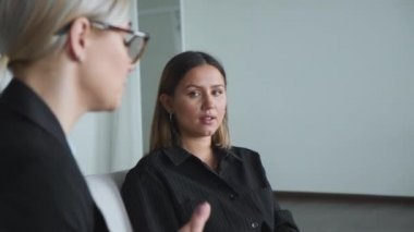 İş toplantısındaki iki kadın yeni bir proje hakkında iş arkadaşlarıyla konuşuyor. İki genç kız sandalyeye oturur ve iş hakkında konuşur. Kızlar gülümser ve iletişim kurar. 