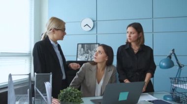 Genç bir iş kadını, modern bir ofisin dinlenme odasında çeşitli meslektaşlarıyla konuşuyor.