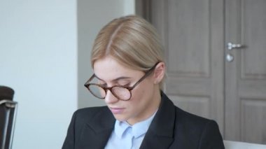Ciddi genç kadın ofiste dizüstü bilgisayarla çalışıyor ve çağdaş odada masa başında oturmuş belgeleri okuyor. Gençlik ve iş kavramı.