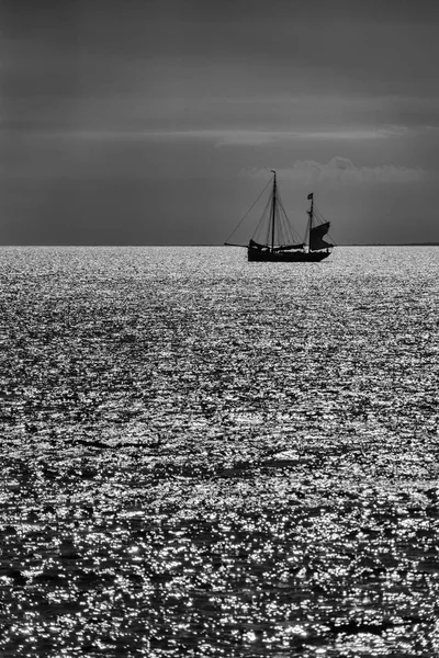 Black and white image of an old fashioned sailing boat against a