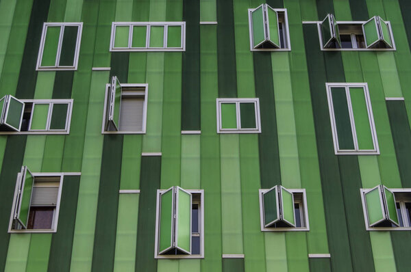 A facade in green tones with windows of different sizes in an apartment building