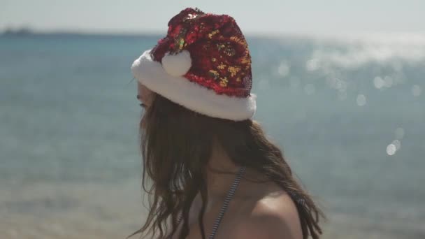 Świąteczna dziewczyna w czerwonym kapeluszu. na czerwonej plaży morskiej — Wideo stockowe