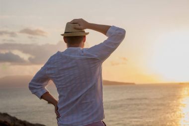 Bir adam beyaz elbise ve şapka silüeti sırtına bir şafak çerçevede güneşin altın ışınları ile denizin üzerinde duruyor