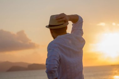 Arkadaki gündoğumu, güneşin parlak altın ışınları denizde çerçevede şapkalı bir adam