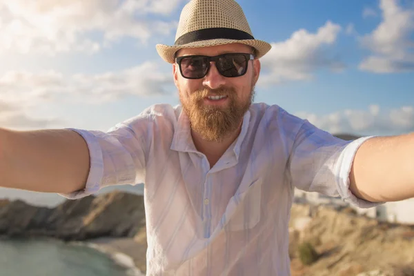 A ginger bearded male hipster traveler is making selfie in the sunny morning with the blue cloudy sky view background