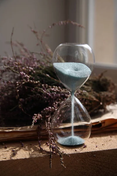 El tiempo pasa, gafas de arena con arena azul, flores, madera — Foto de Stock