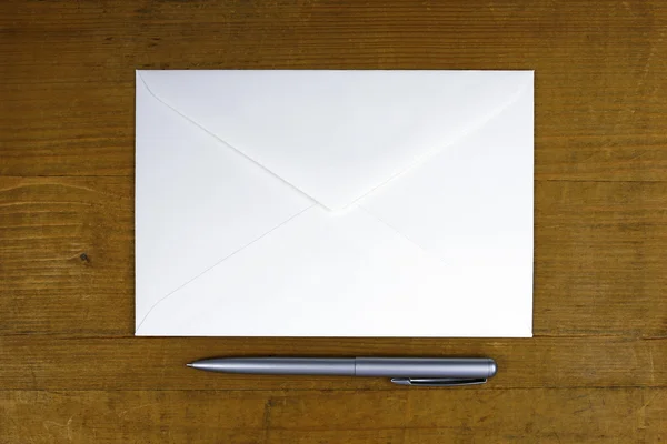 Envelope branco e caneta sobre fundo de madeira — Fotografia de Stock