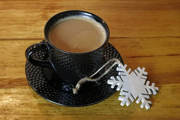 Tasse heißen Kaffee und Weihnachtsstern mit Schneeflocken auf Holztisch — Stockfoto